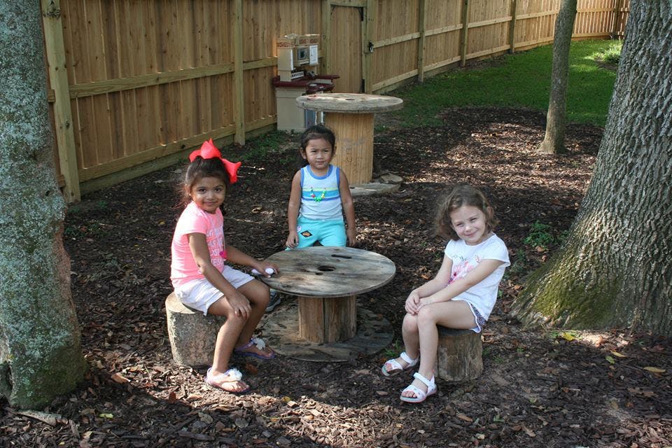 Three children sitting and standing around a wooden spool table outdoors