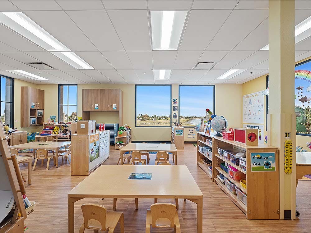 Empty classroom with small tables and chairs, shelves, and large windows