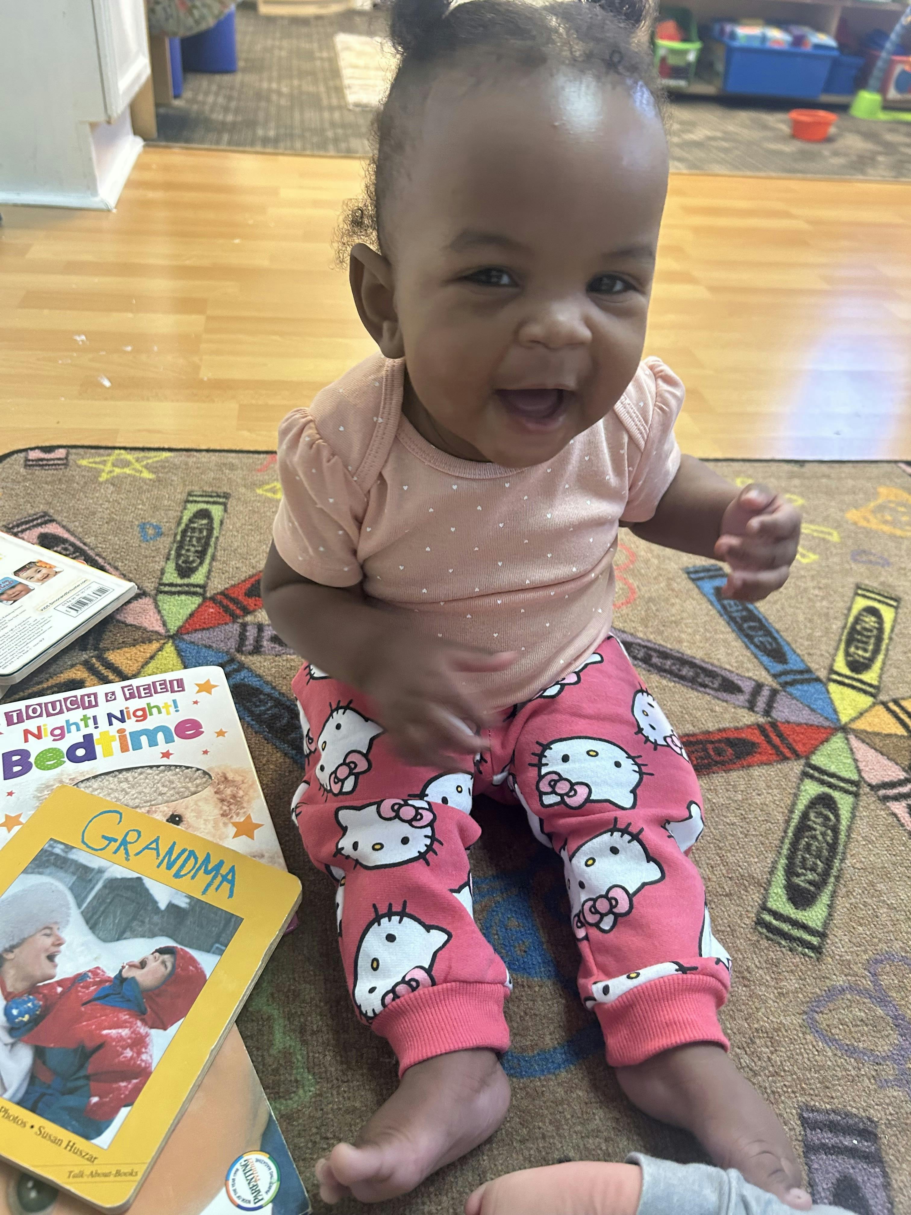 Child in pink pajamas sitting on a crayon-themed rug with books