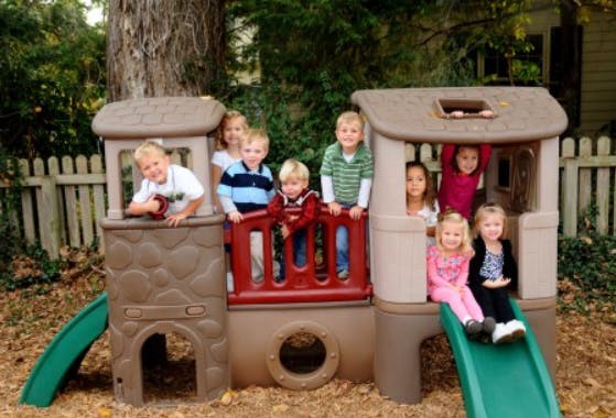Group of children playing on an outdoor playset with slides and a playhouse