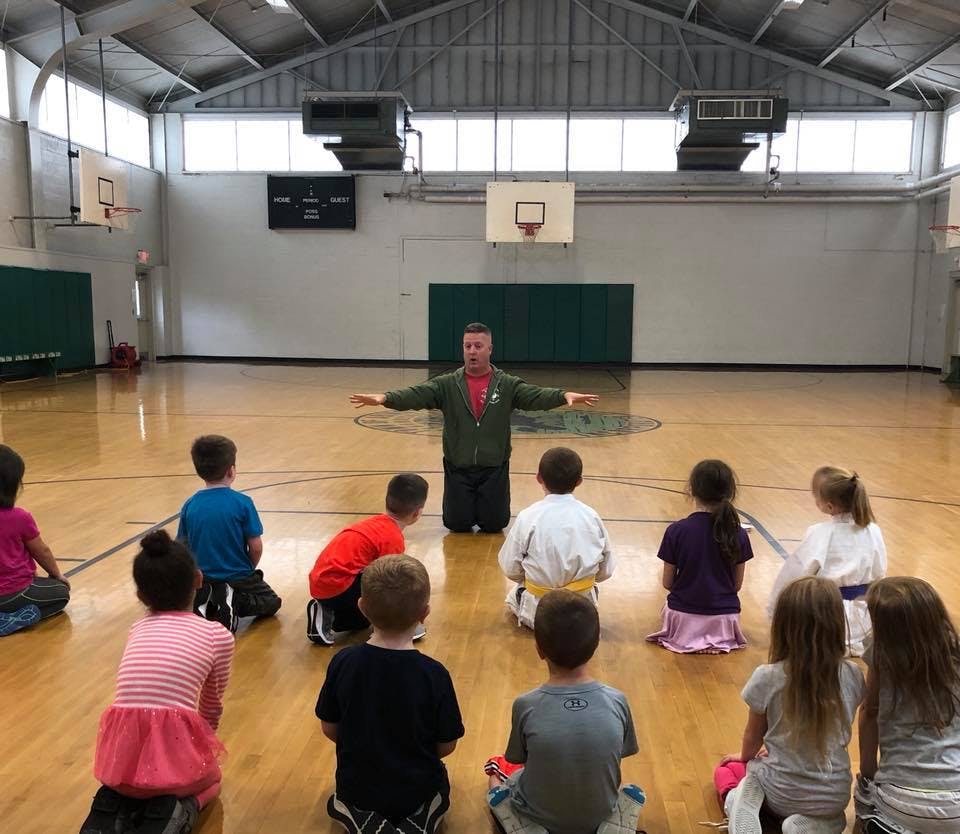 Adult leading a group of children sitting on a gym floor