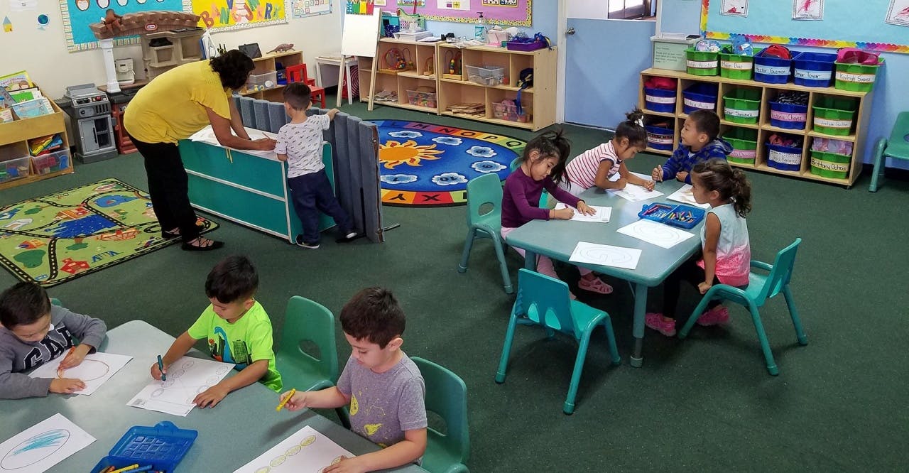 Adult and children in a classroom drawing and children drawing at tables
