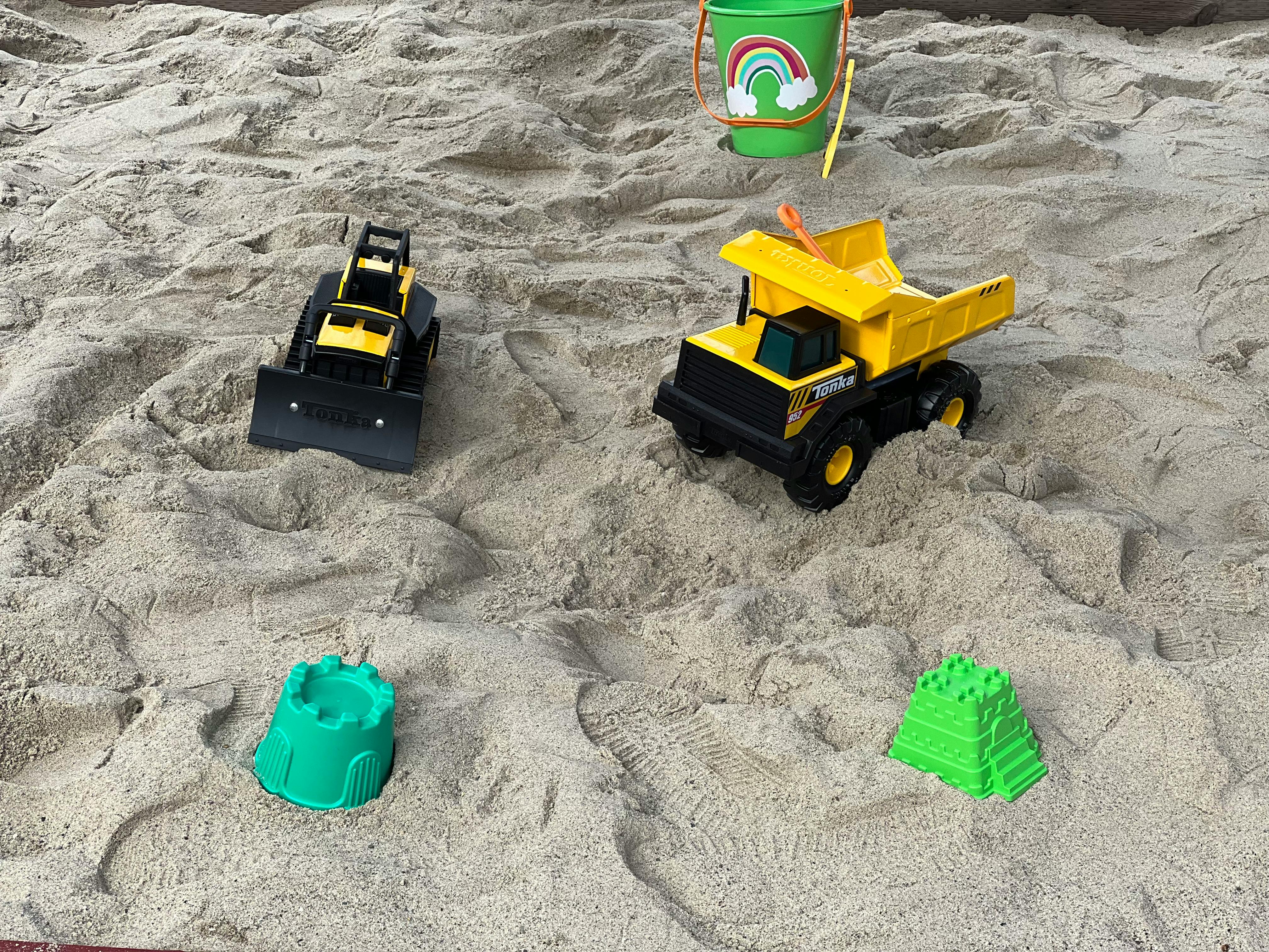 Toy dump truck, bulldozer, bucket, and sand molds in sand