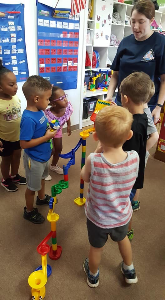 Adult and children playing with a marble run toy in a classroom