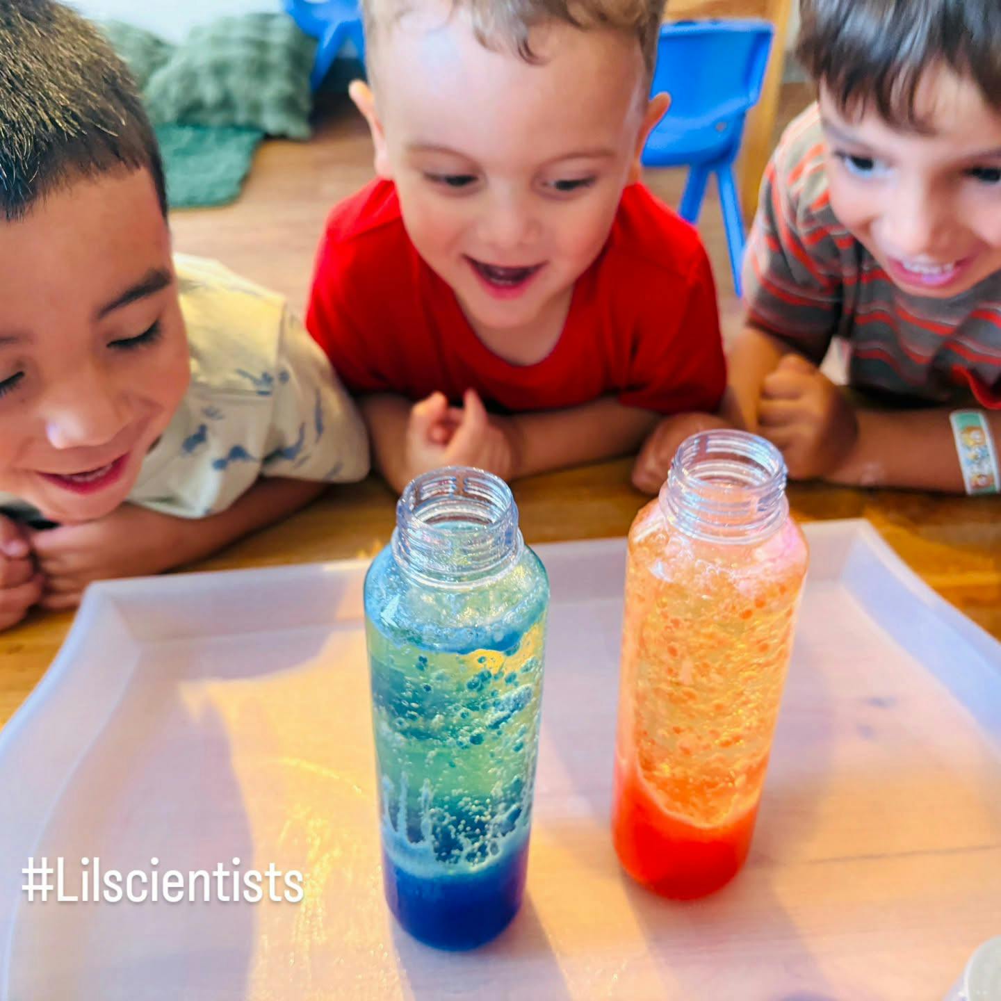Three children observing two science bottles on a tray
