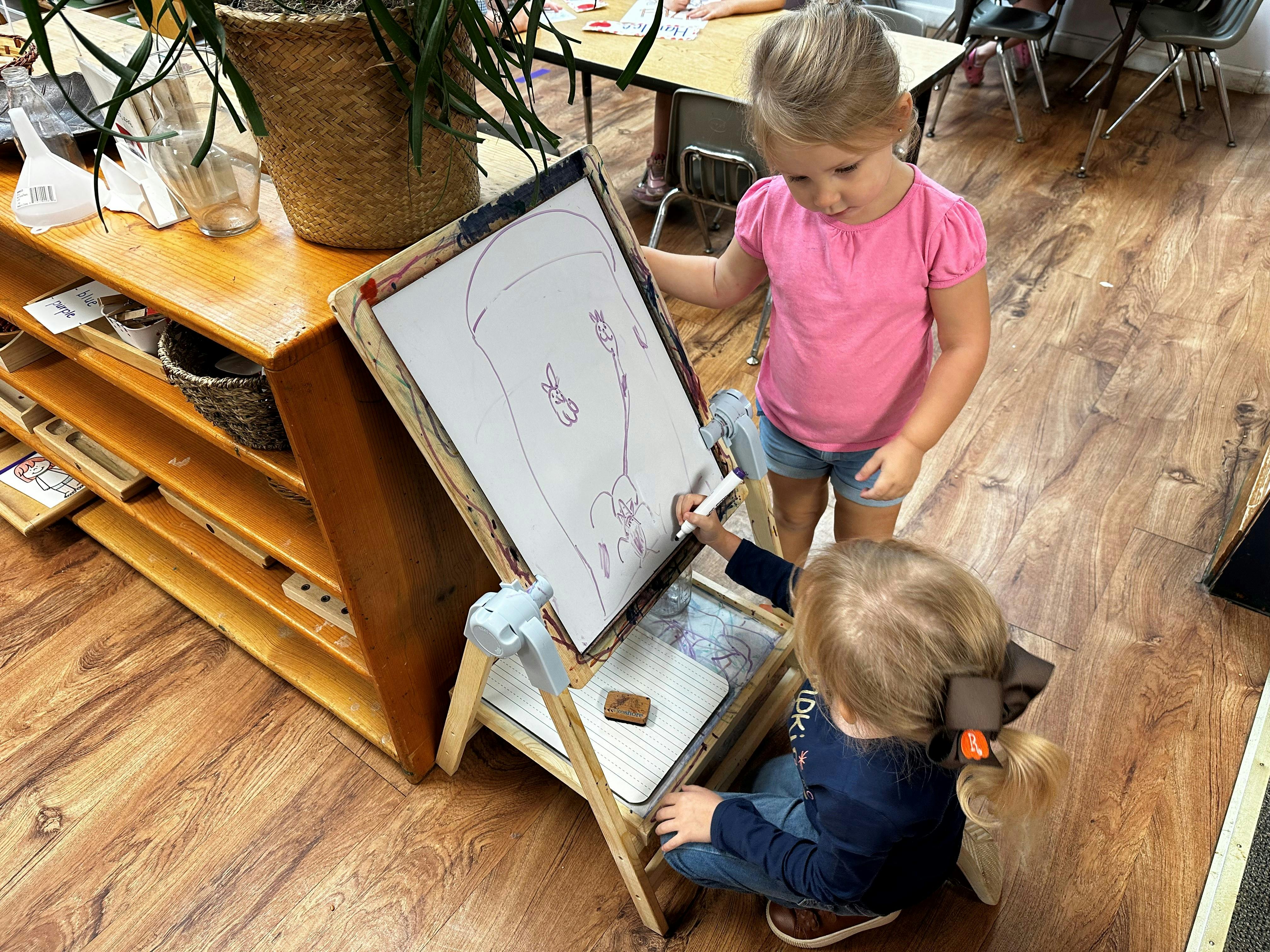 Two children drawing on an easel in a classroom