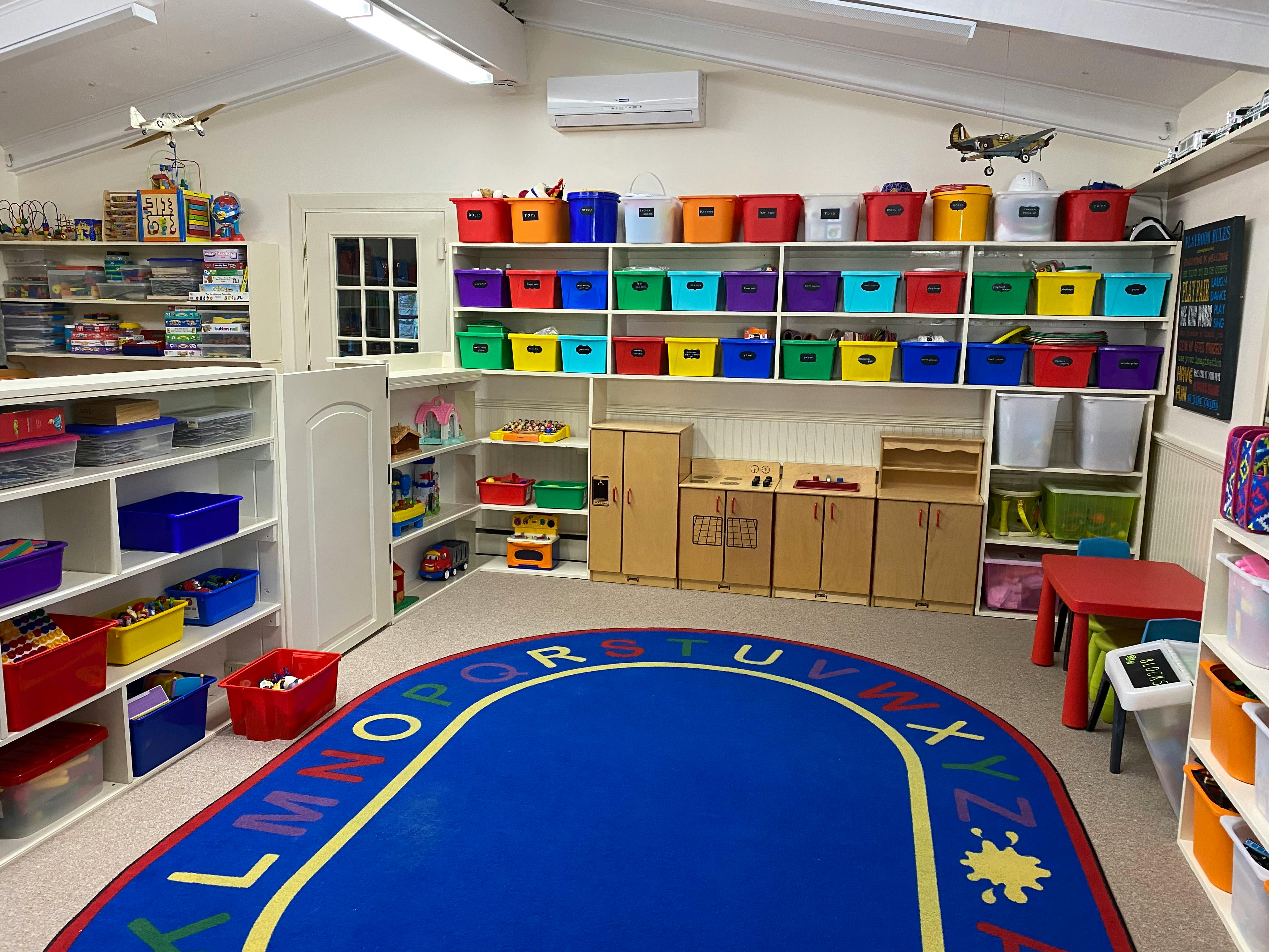 Classroom with shelves of colorful bins and a blue alphabet rug