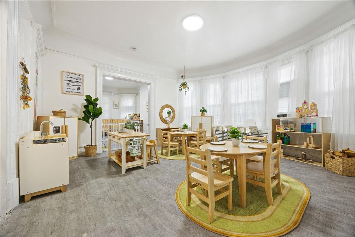 Childcare room with small wooden tables and chairs and toy kitchen set