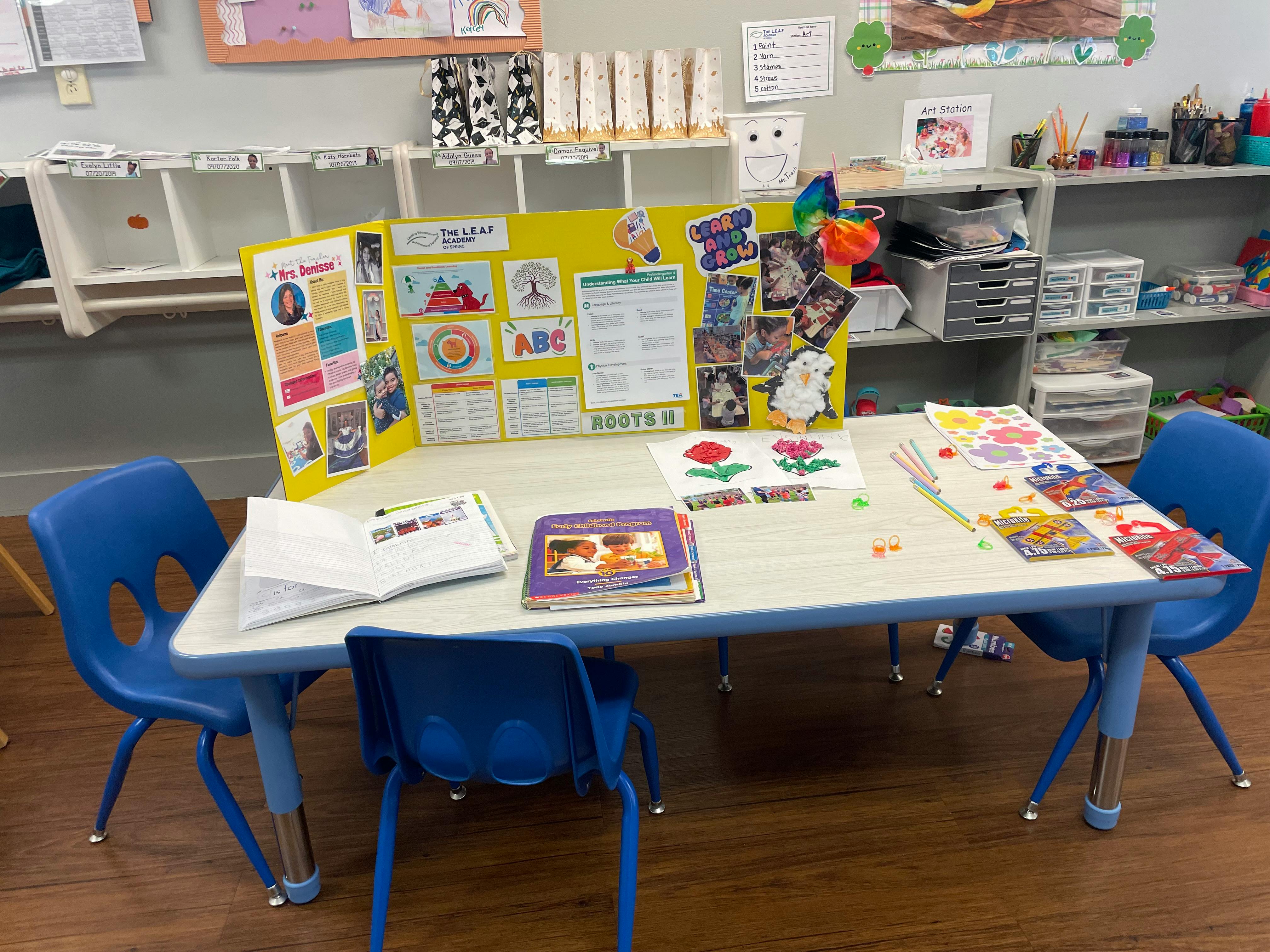 Classroom table with blue chairs, books, and a yellow display board