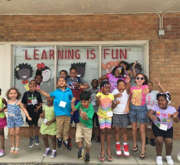 Group of children jumping in front of a window with "LEARNING IS FUN" text