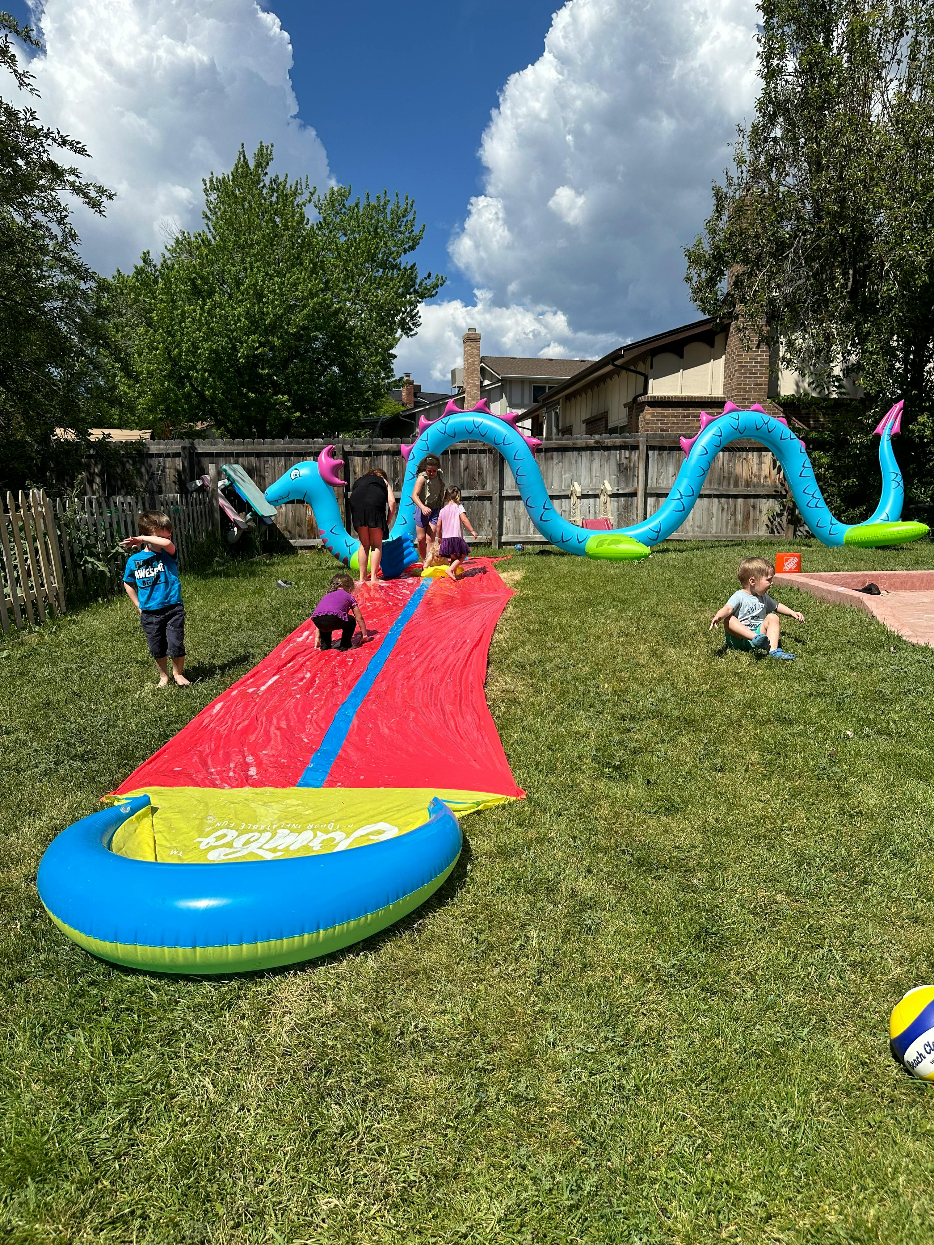 Children playing on a large inflatable water slide in a backyard
