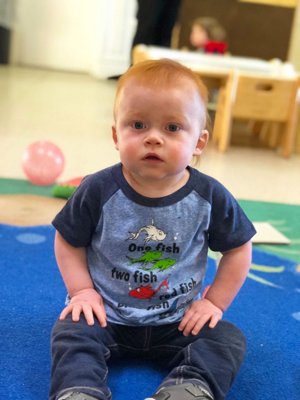 Child sitting on a blue rug in a classroom