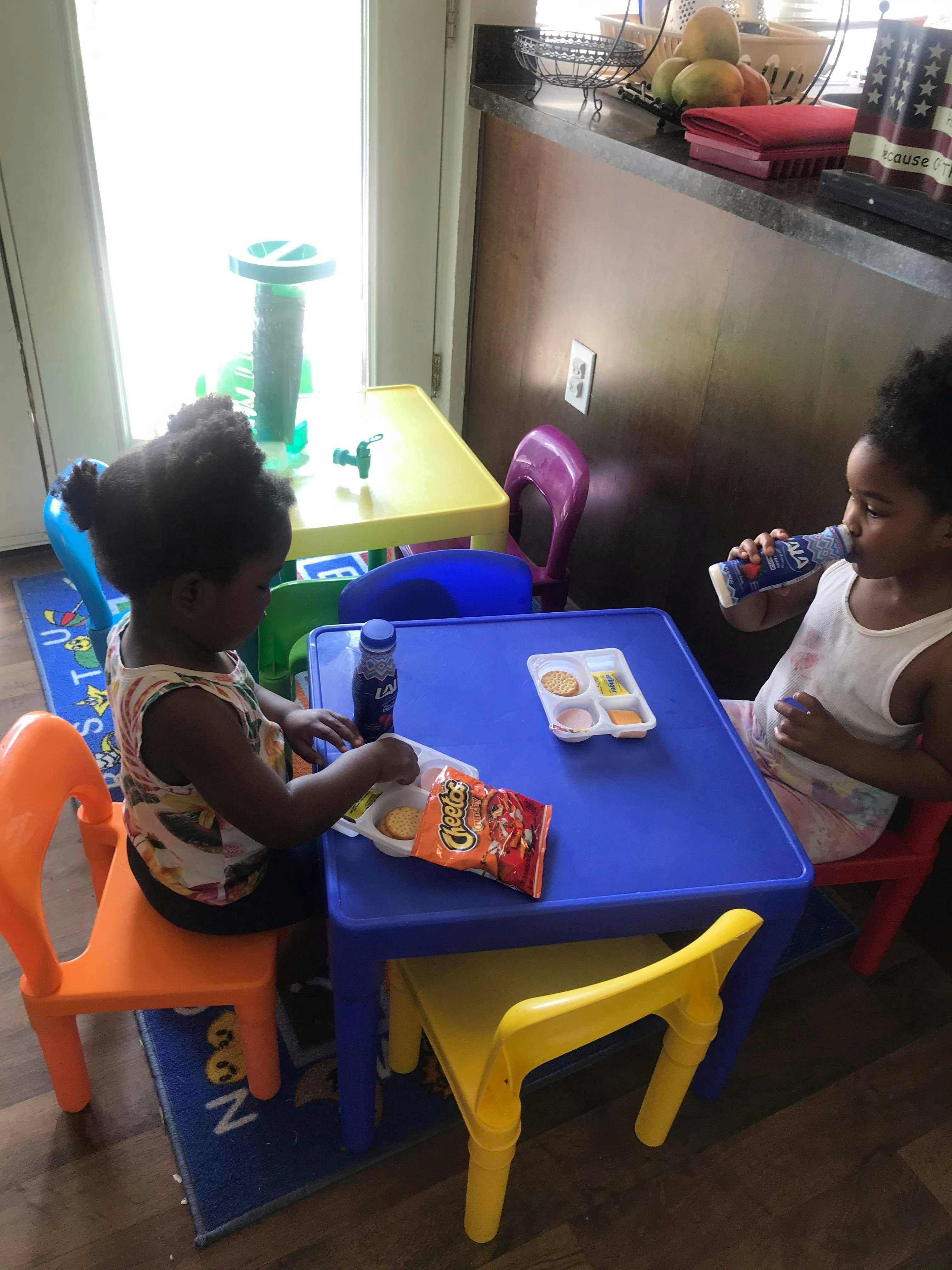 Two children sitting at small tables eating snacks