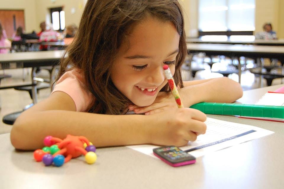 Child writing on paper with a pencil in a classroom