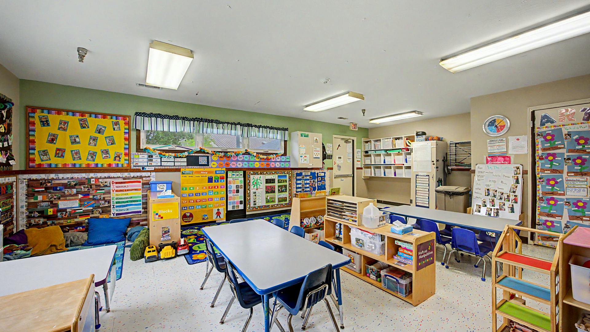 An empty preschool classroom with tables, chairs, and learning materials