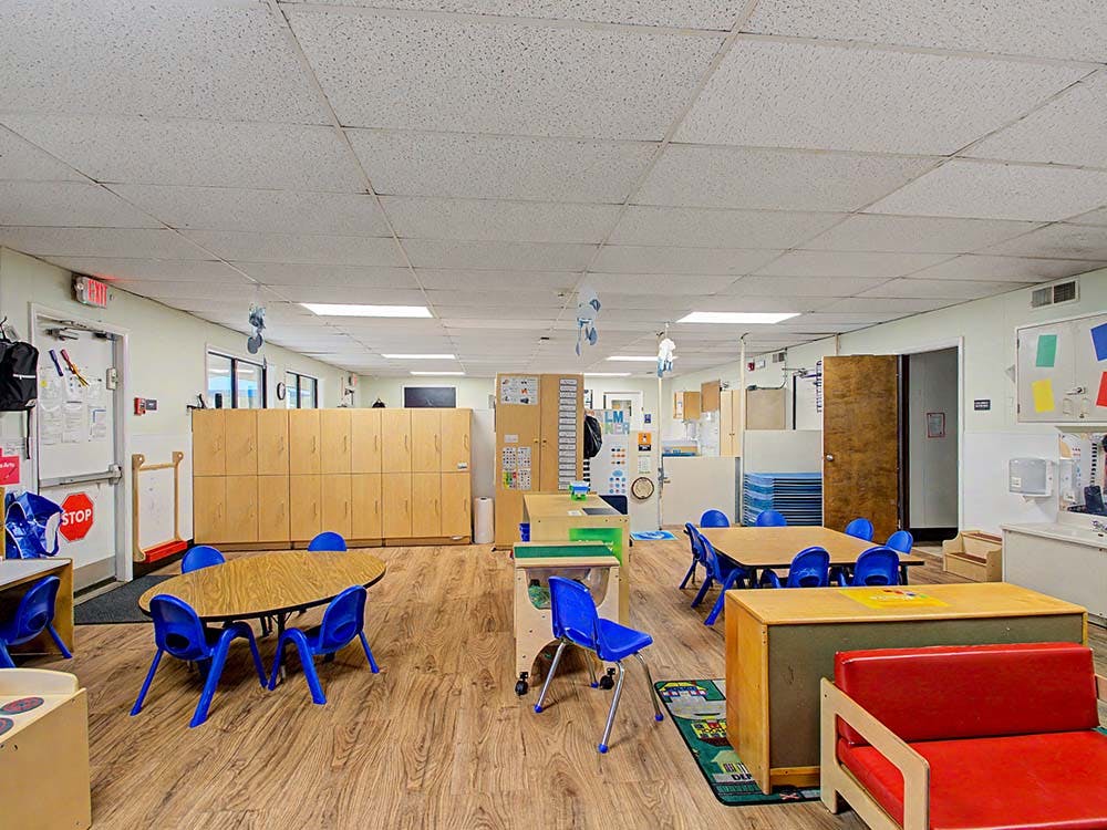 Empty classroom with small tables and chairs, lockers, and play furniture