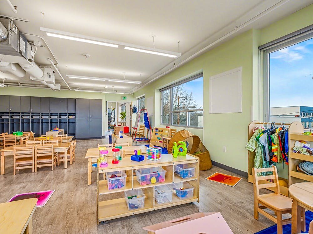 Empty classroom with small wooden tables and chairs, storage cubbies, and toys