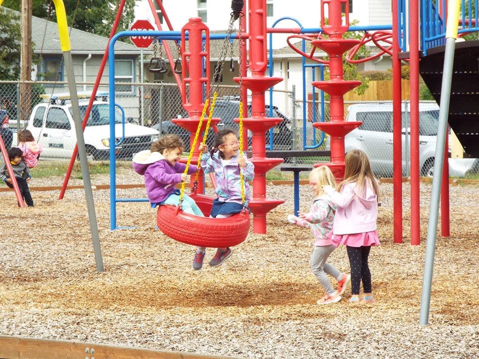 Children playing on a tire swing and standing on a playground