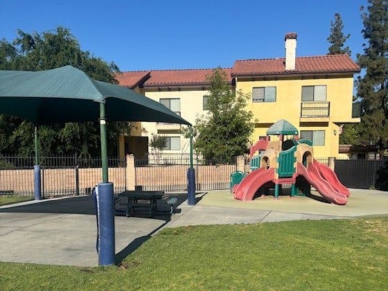 A playground with slides and a covered picnic area next to a building