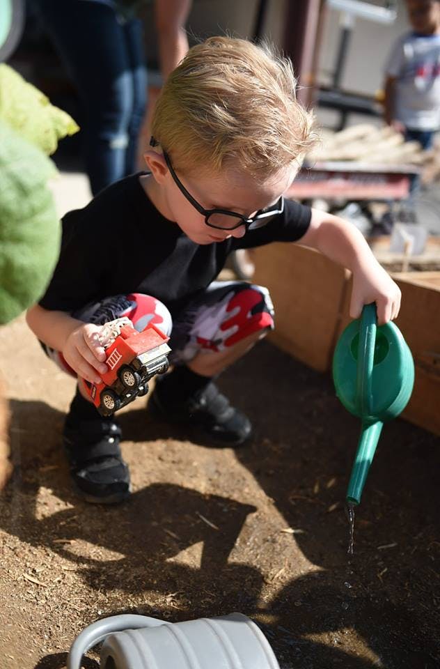Child in glasses holding a toy truck and watering can