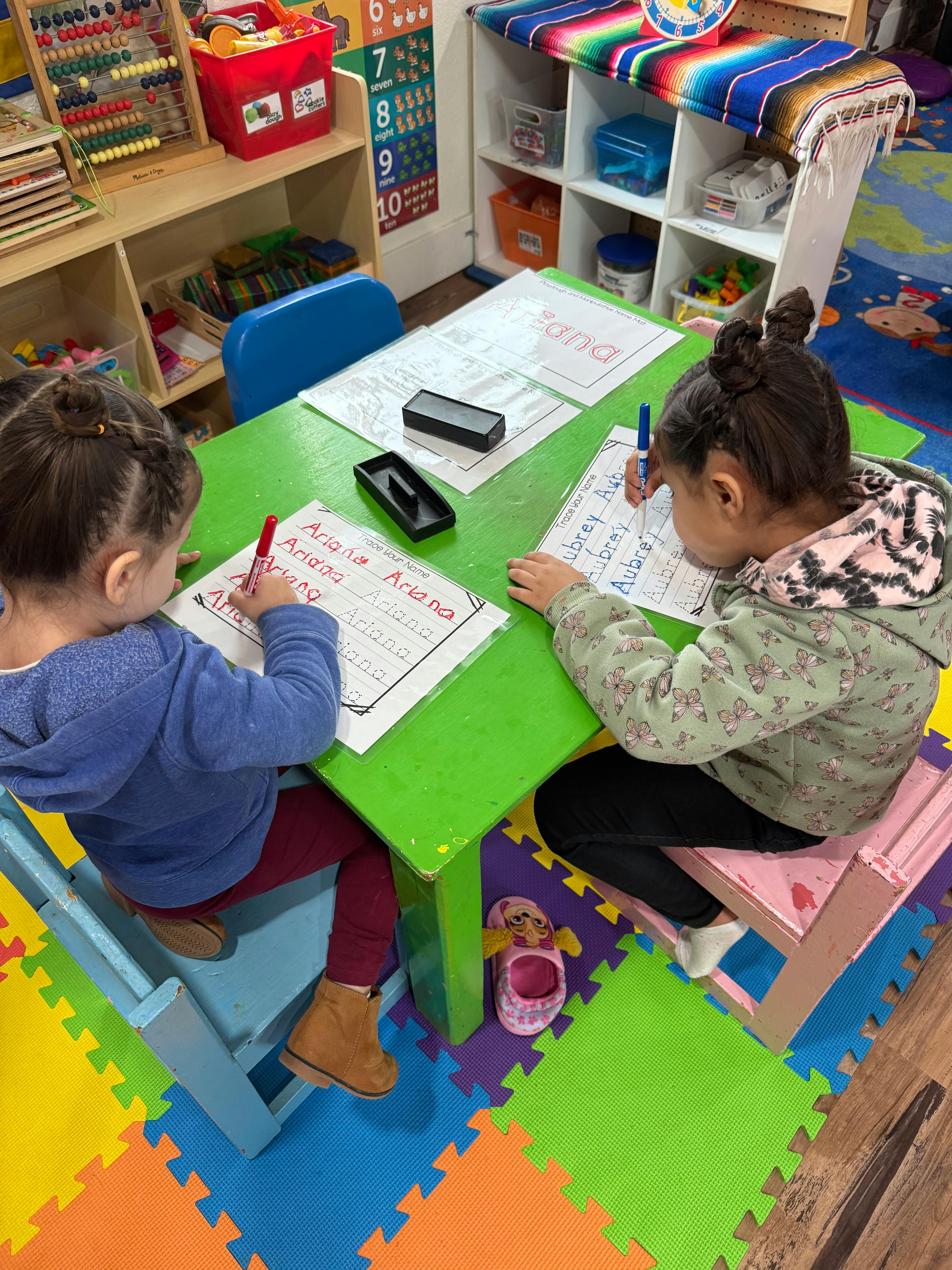 Two children writing at a green table in a classroom