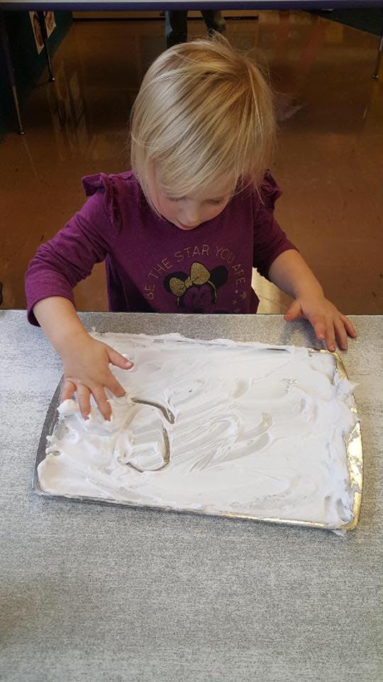 Child playing with shaving cream on a tray