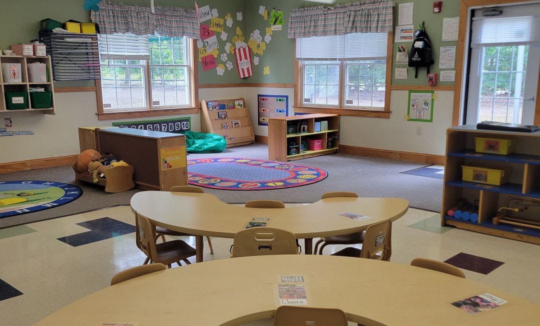 Empty classroom with children's tables and chairs, bright walls, and large windows