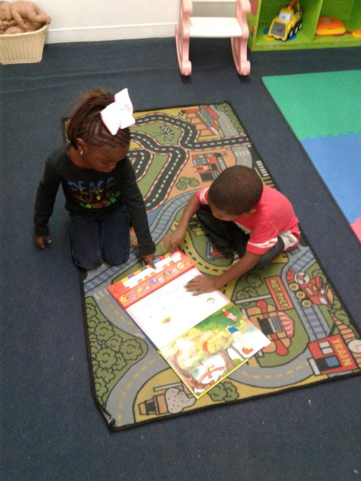 Two children kneeling on a rug looking at a book