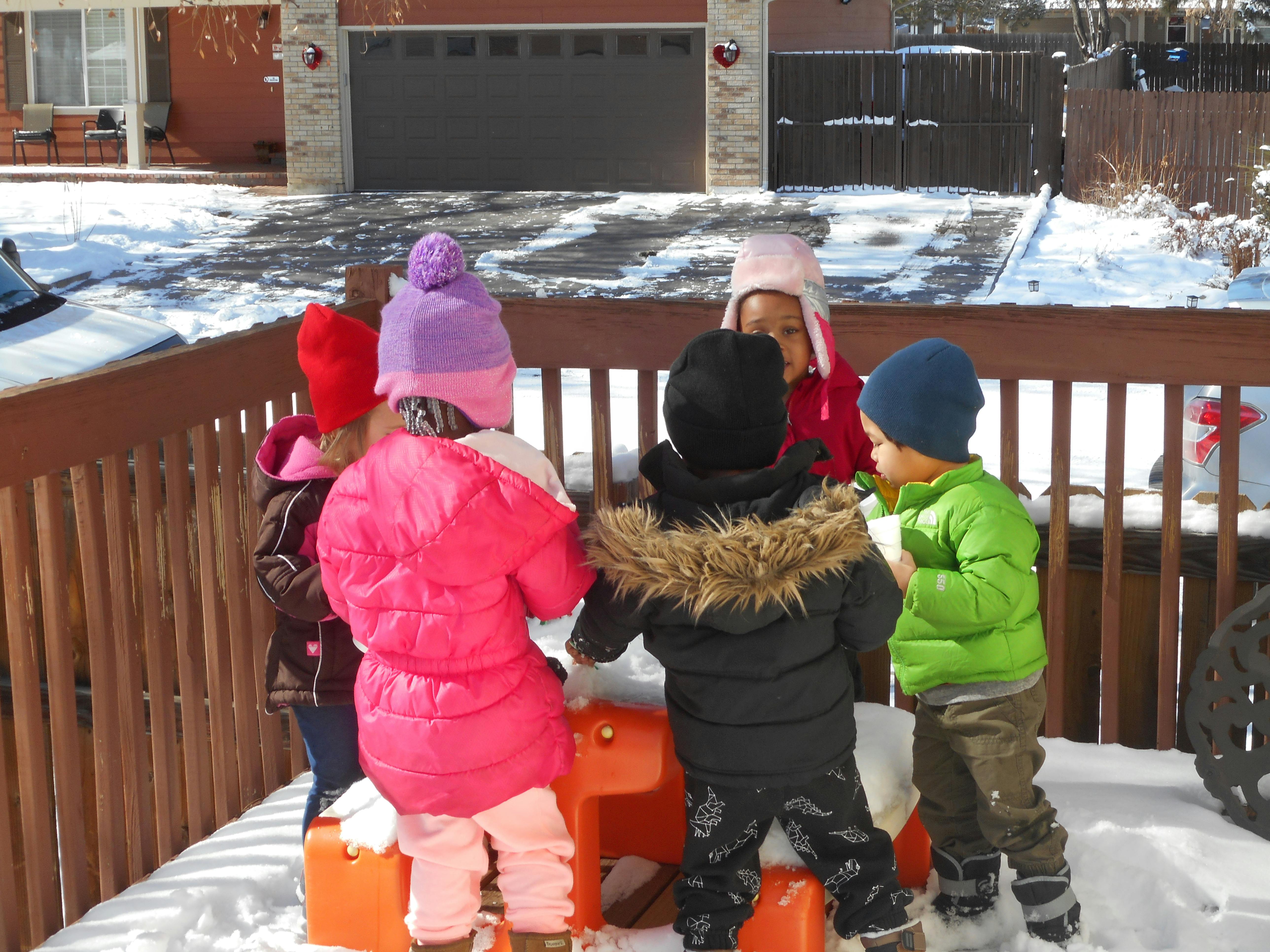 Children in winter clothing playing in snow on a deck