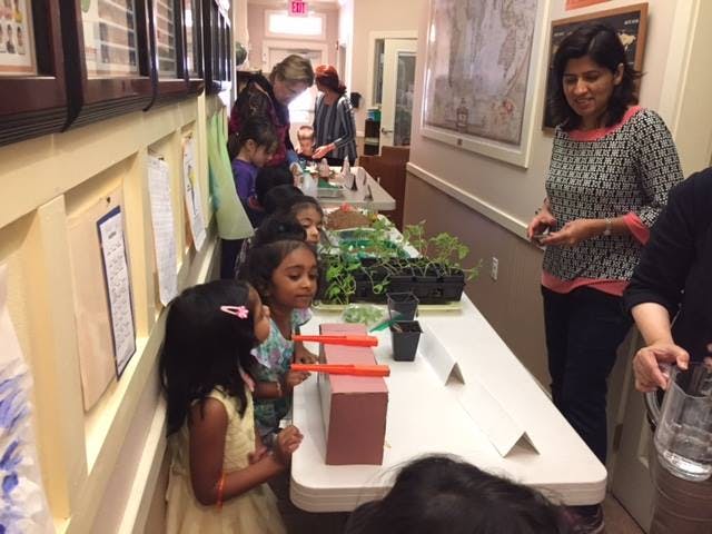 Children and adults gathered around a table with plants and science experiments