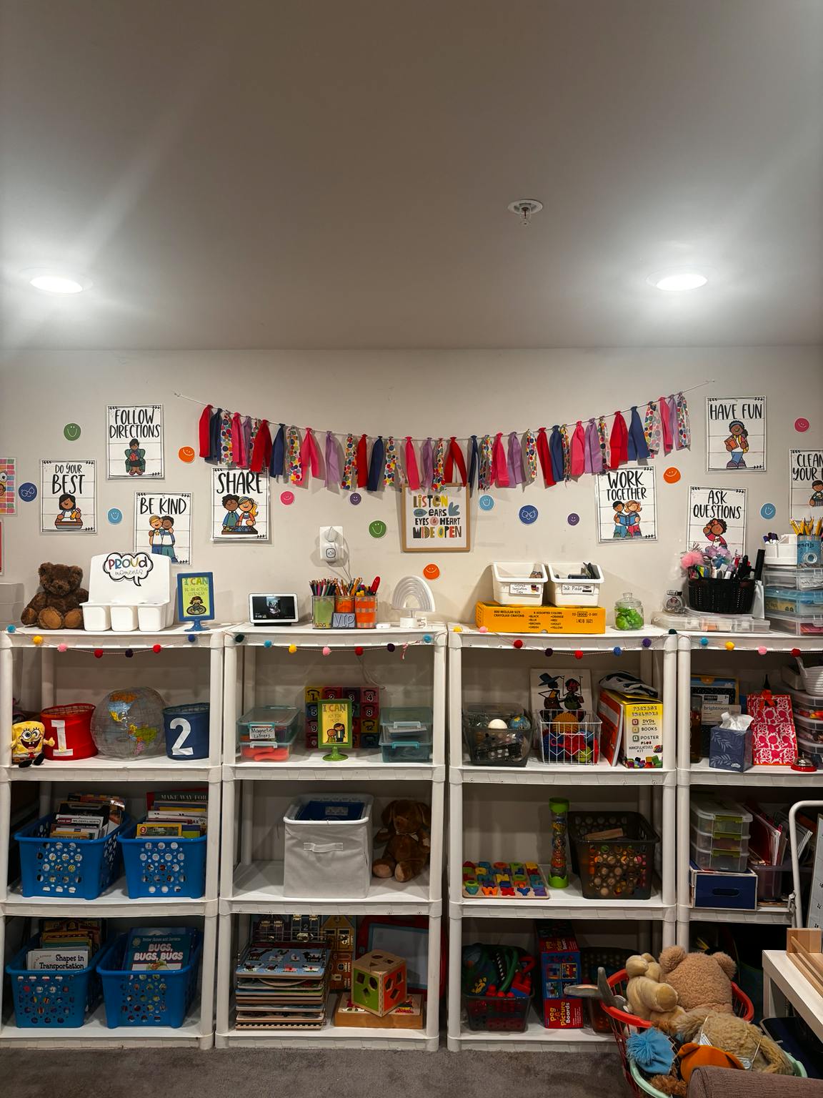 Classroom shelves filled with books and toys under educational wall posters