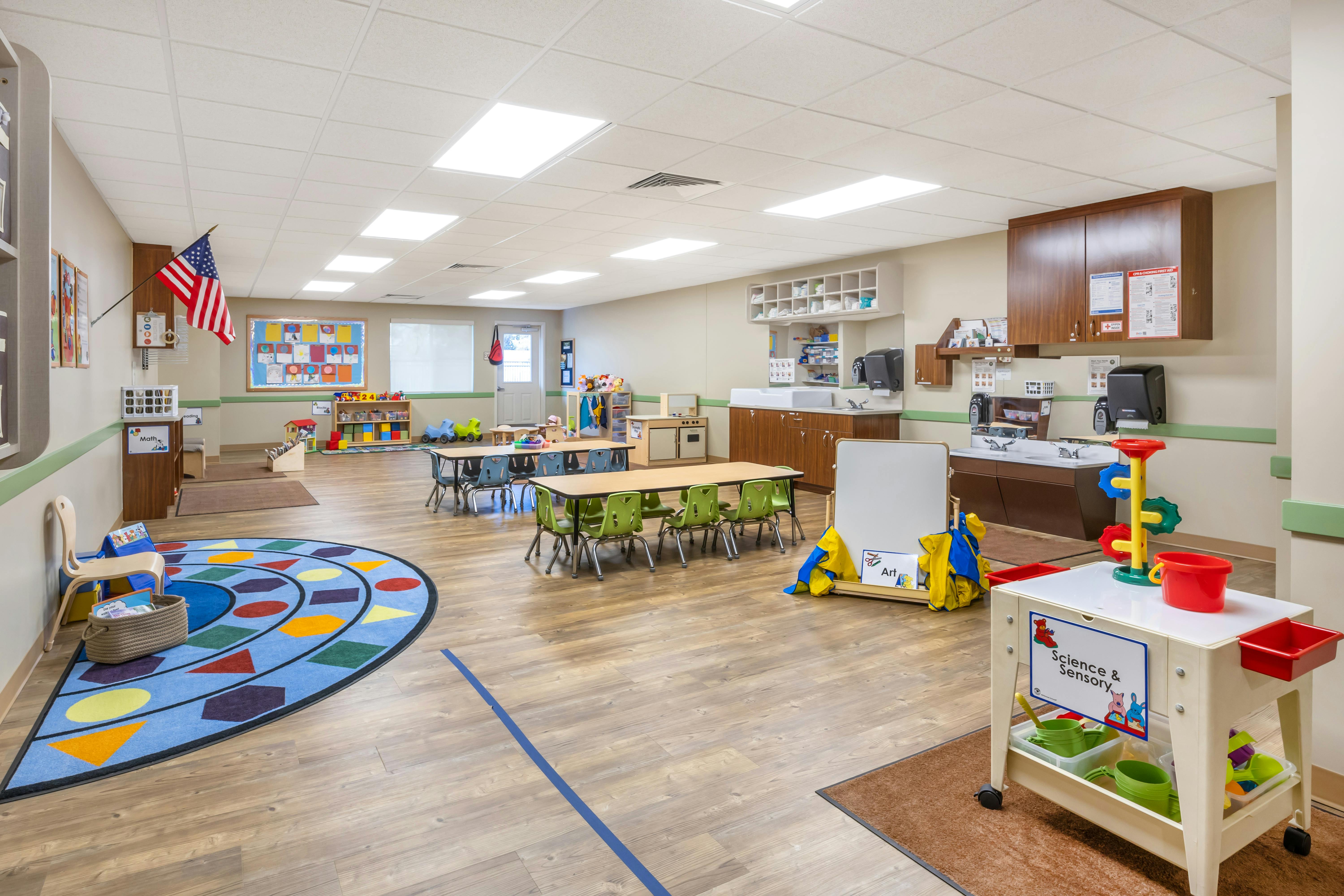 An empty early childhood classroom with small tables and chairs