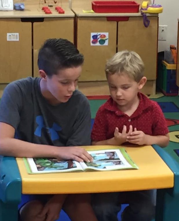 Teen and child reading a book together at a table