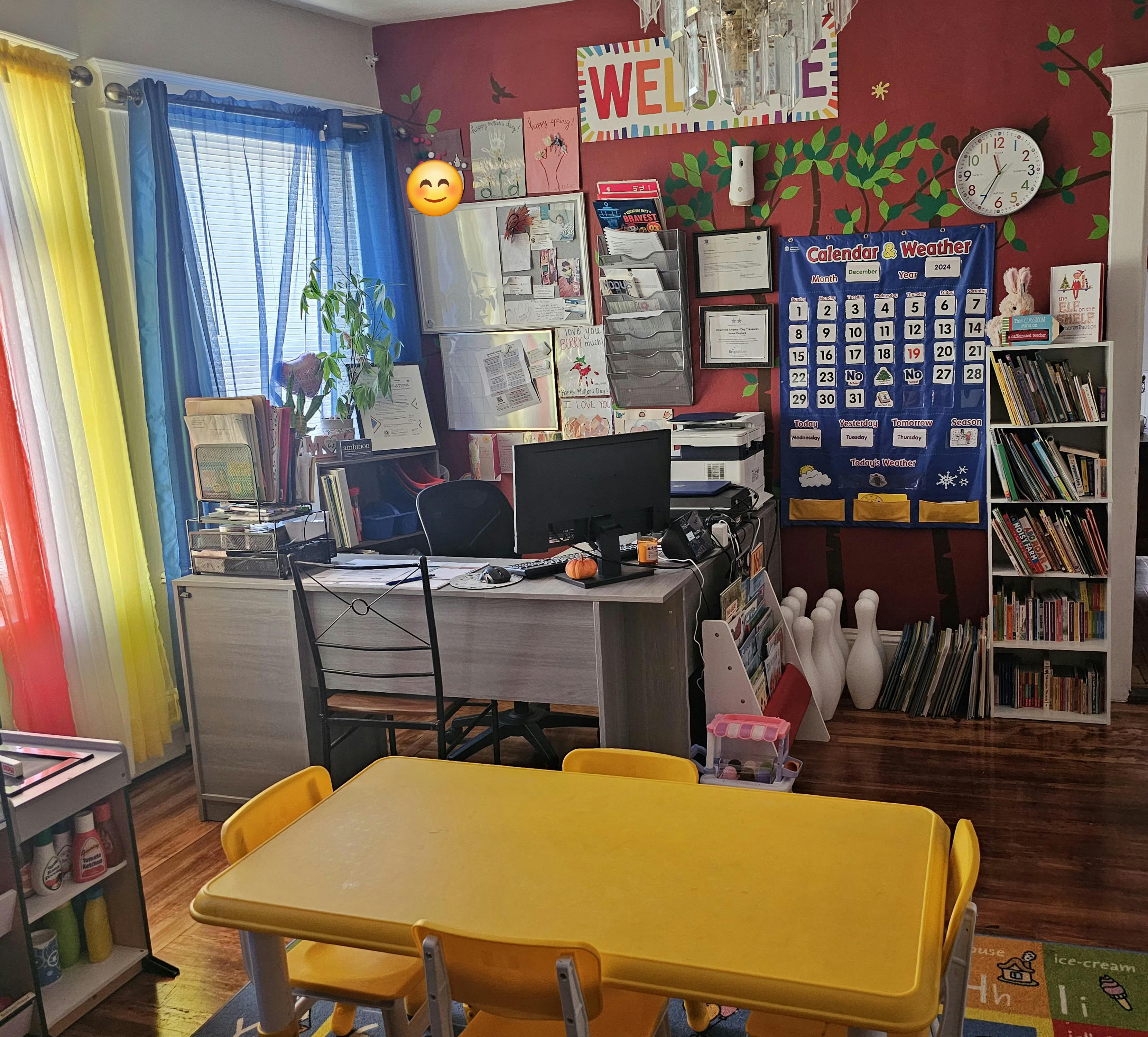 Classroom with a yellow table and chairs, desk with computer, and bookshelves