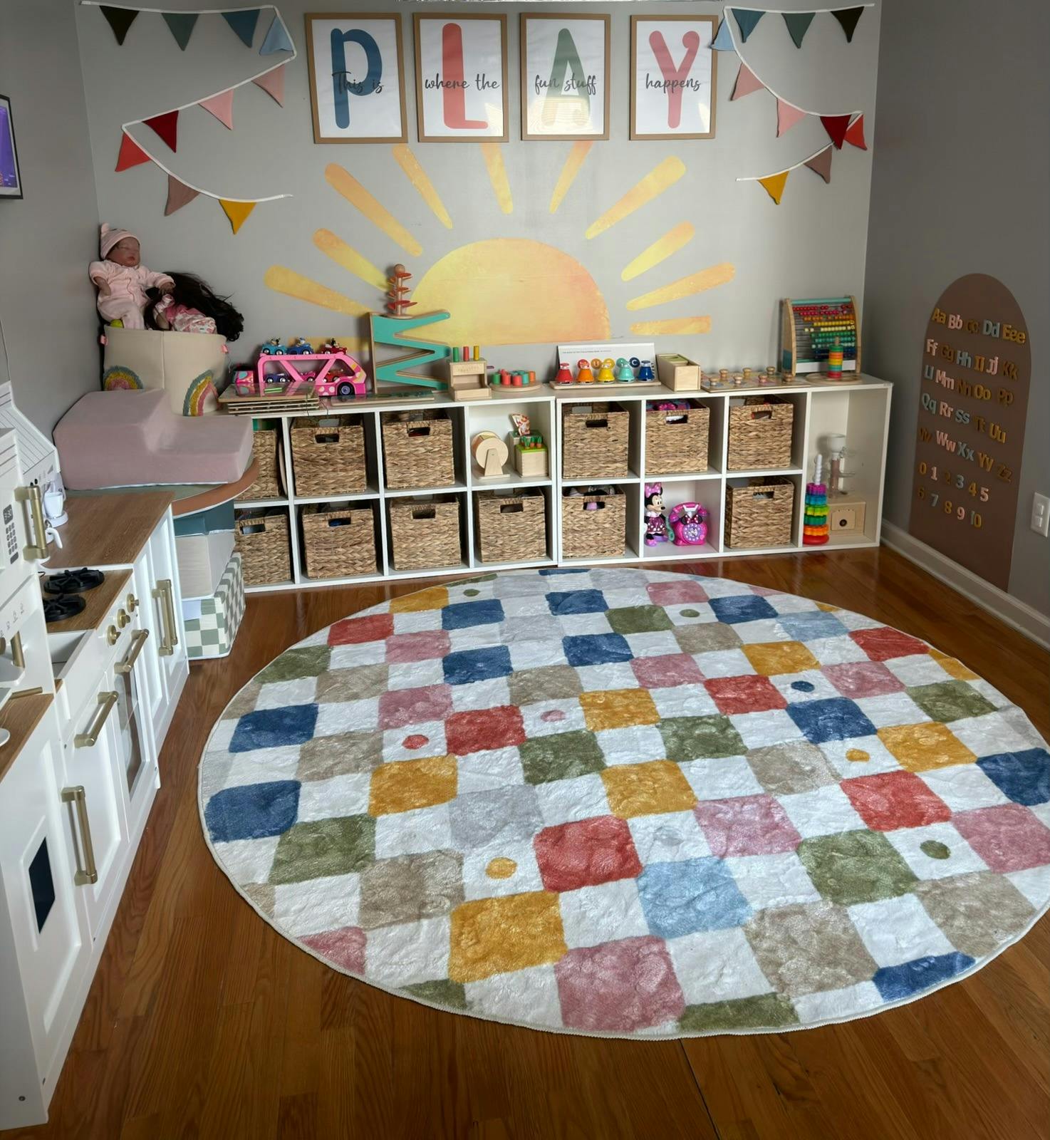 Playroom with a round checkered rug, toy storage shelves, and a toy kitchen