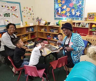 Two adults and three children reading a book in a classroom