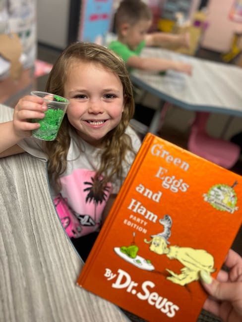Child holding a cup of green sprinkles next to a Dr. Seuss book