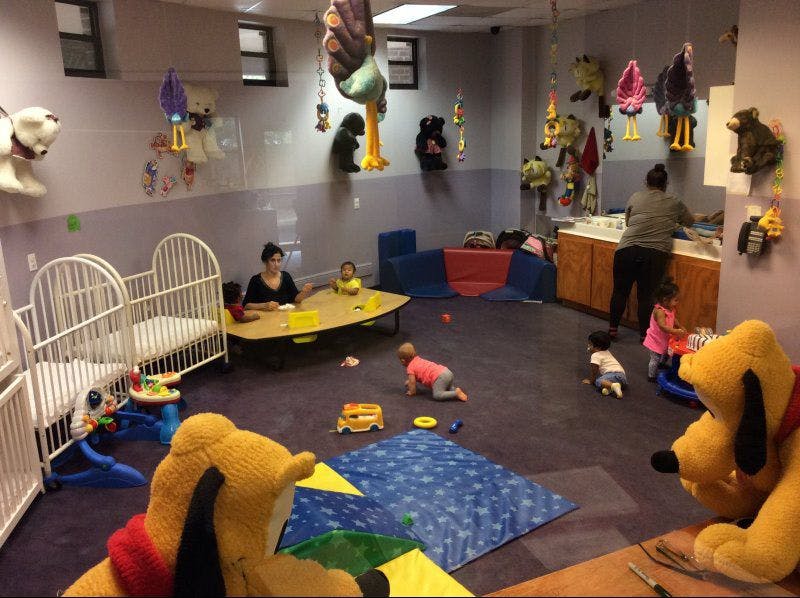 People and children in a playroom with toys and cribs