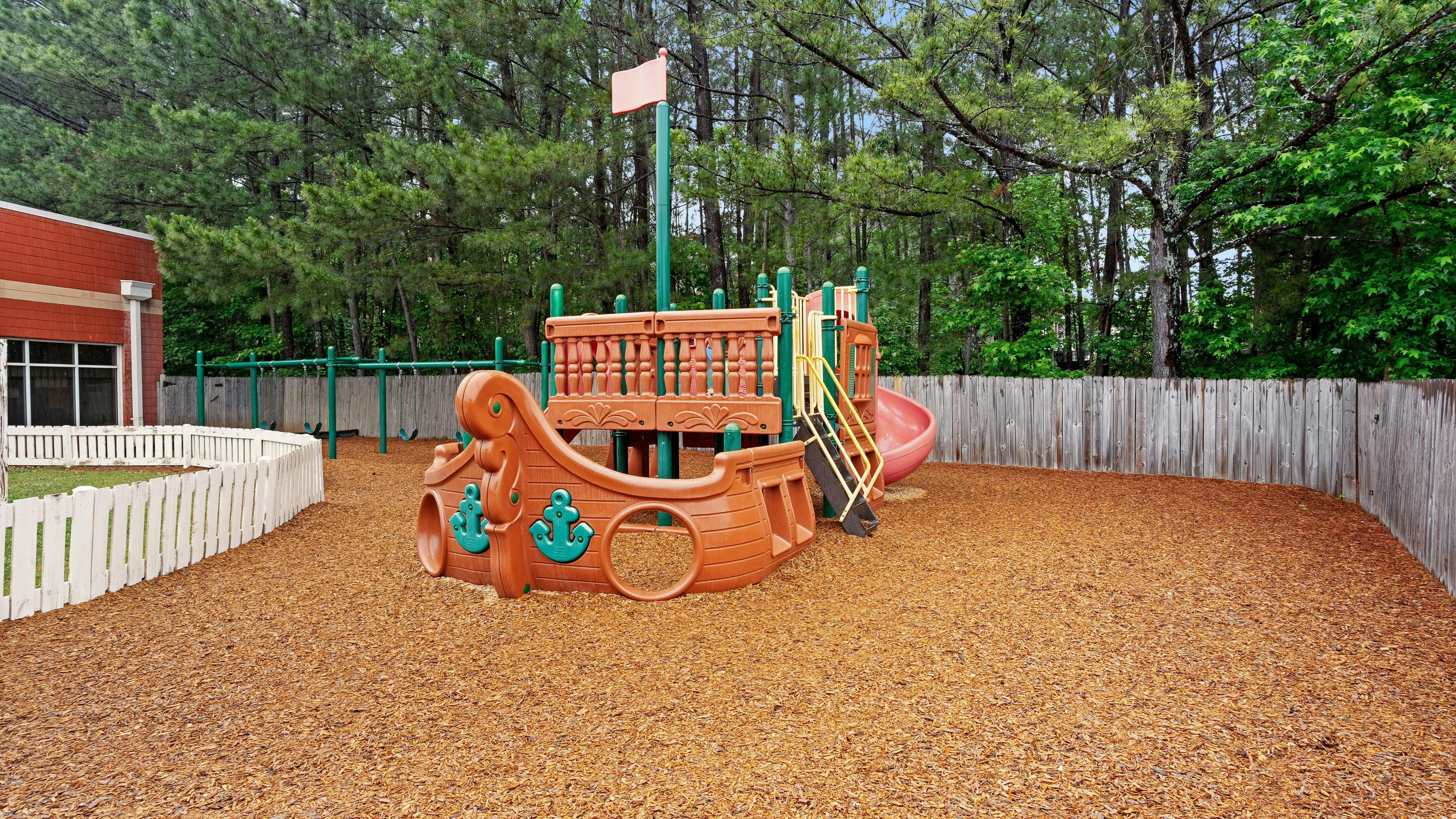 A playground with a ship-shaped play structure and a slide on wood chips