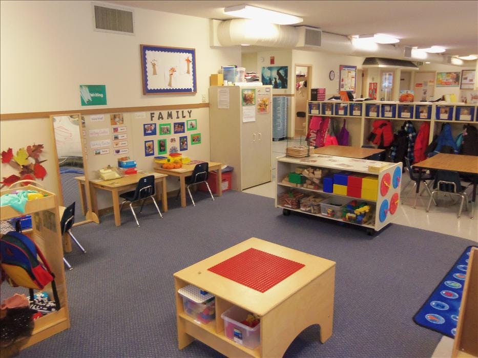 Classroom with small tables, chairs, shelving units, and coats hanging in cubbies