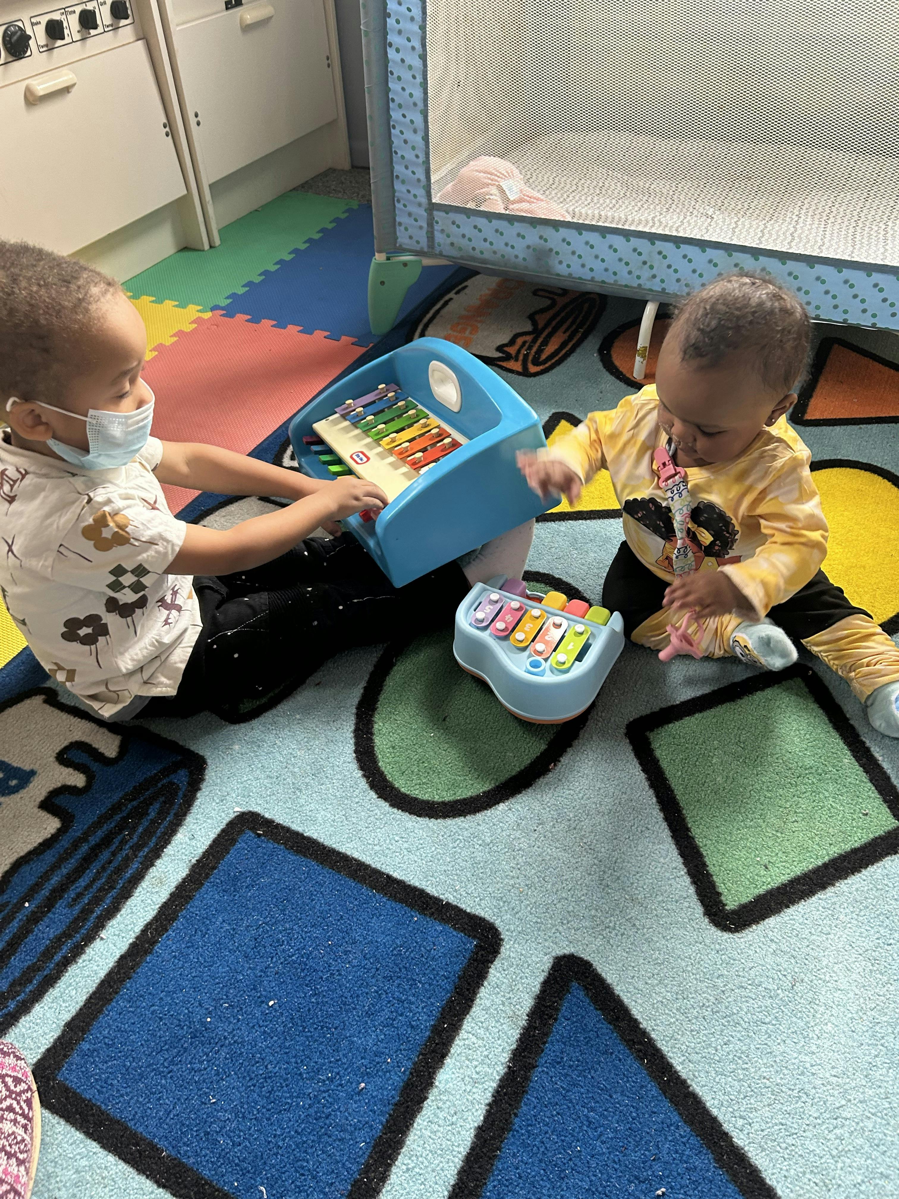 Two children playing with xylophones on a colorful rug