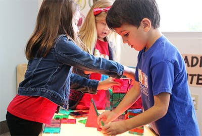 Three children playing with colorful magnetic blocks on a light table