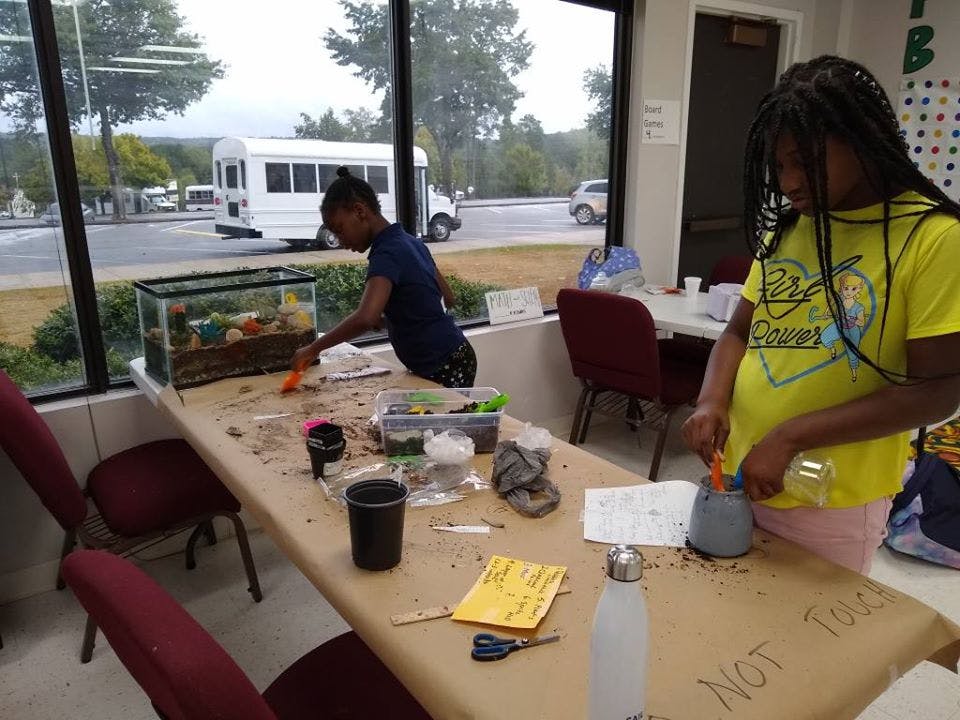 Two children working at a table with a terrarium and craft supplies