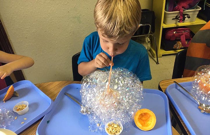 Child blowing bubbles through a straw into a tray