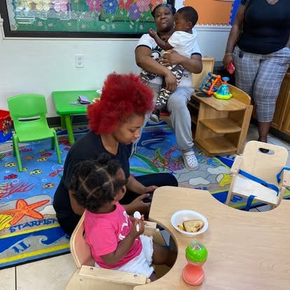 People in a classroom with a child eating at a small table