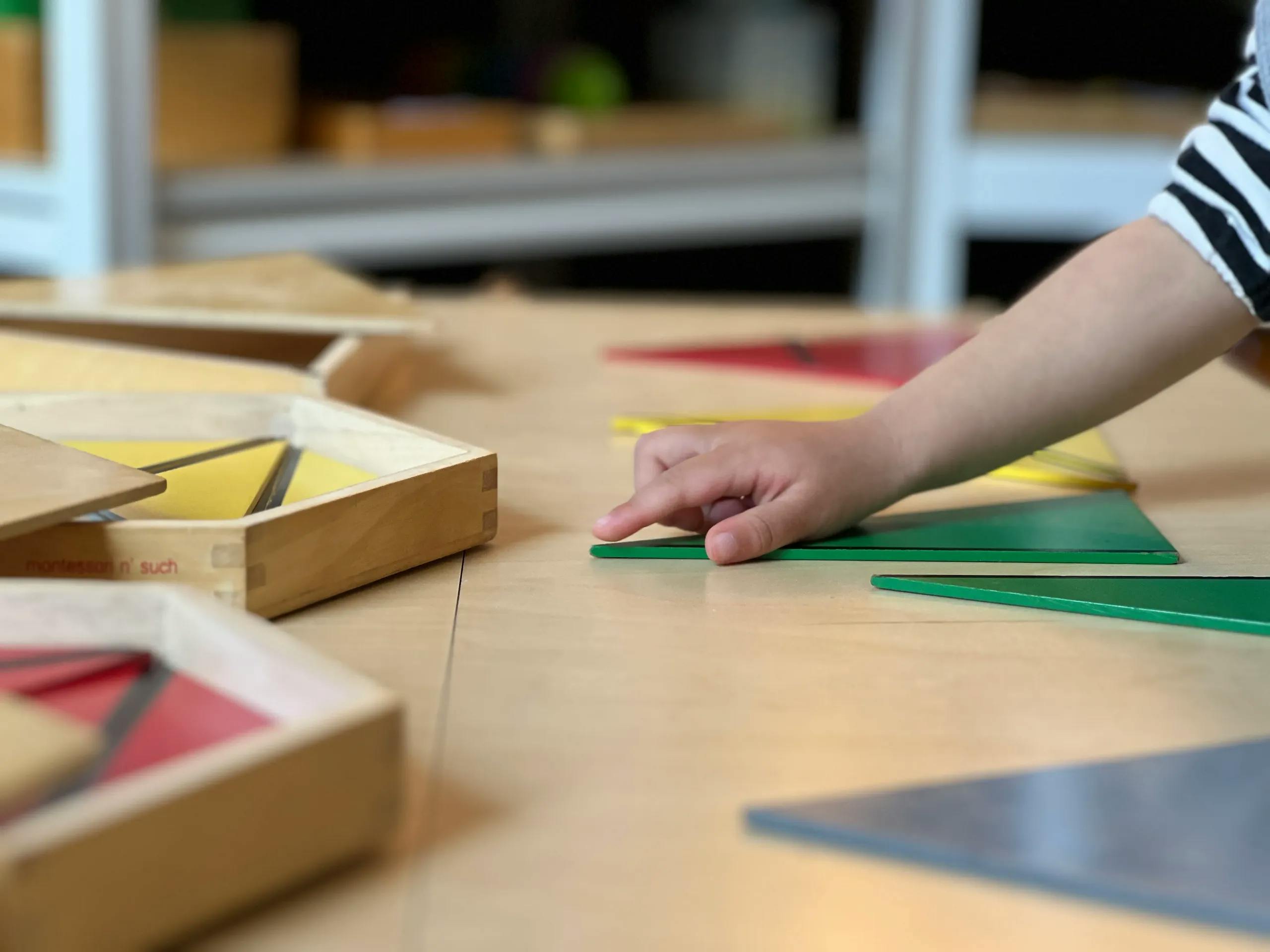 Child's hand touching a green triangle on a wooden table