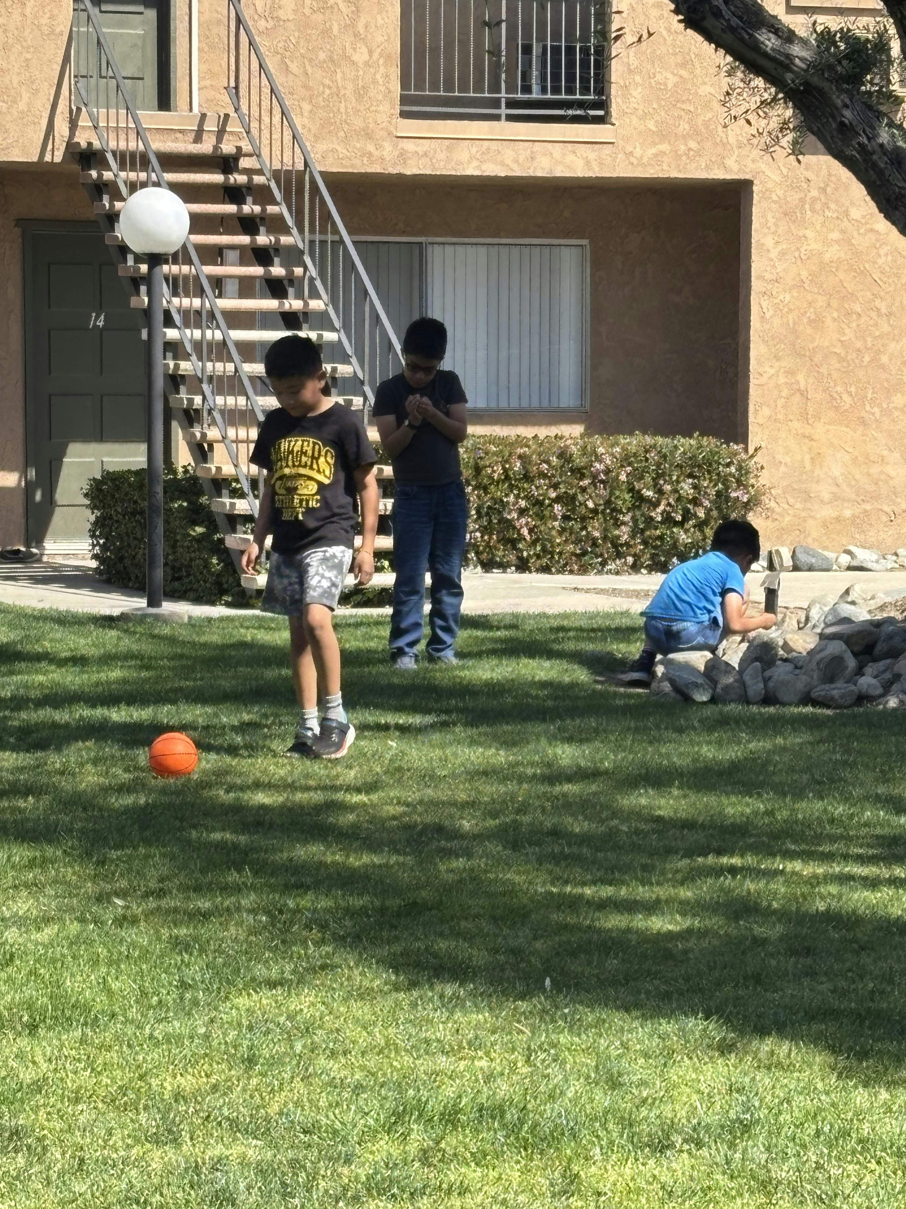 Three children playing on grass near an apartment building