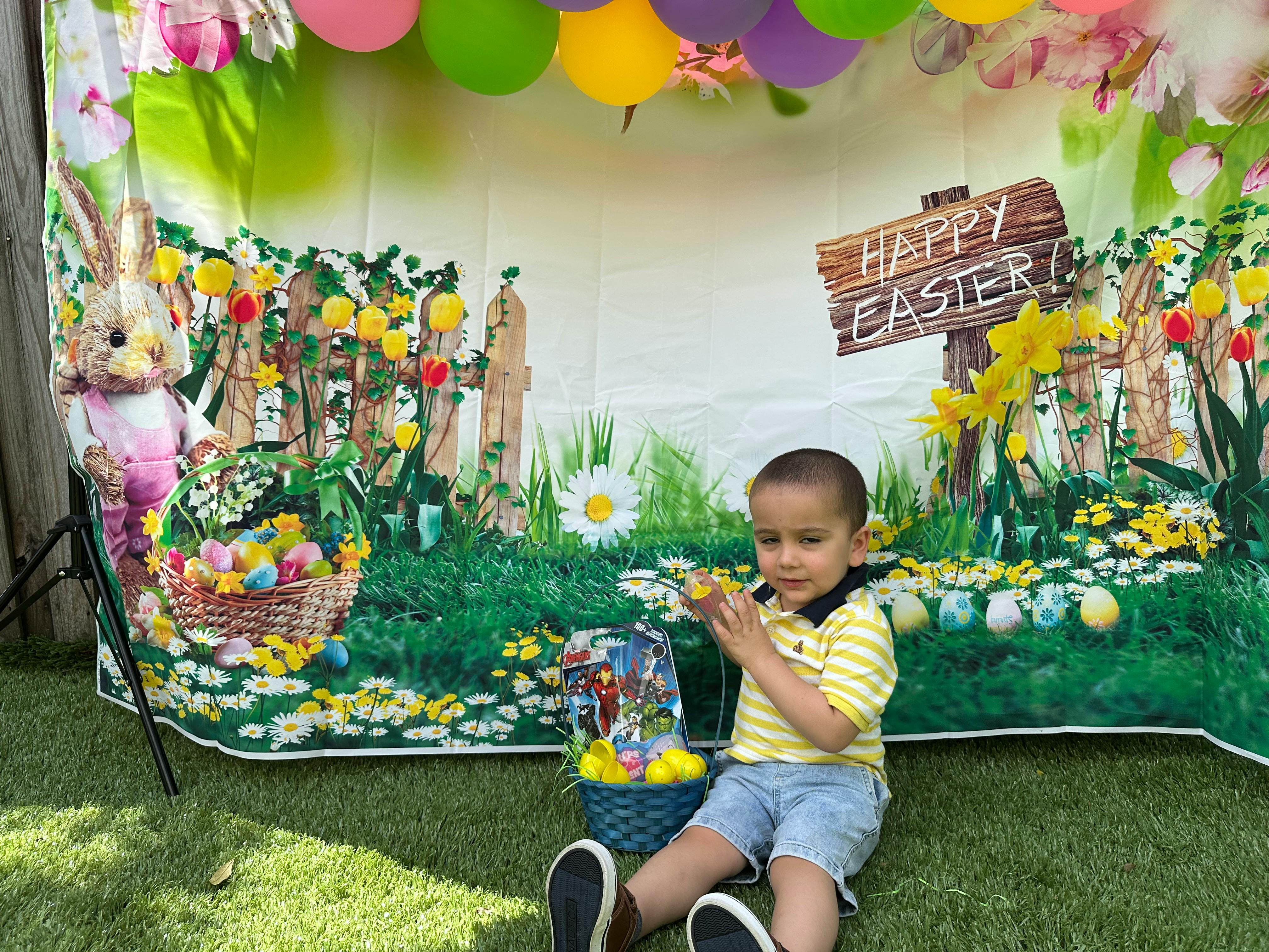 Child sitting on grass in front of a Happy Easter backdrop