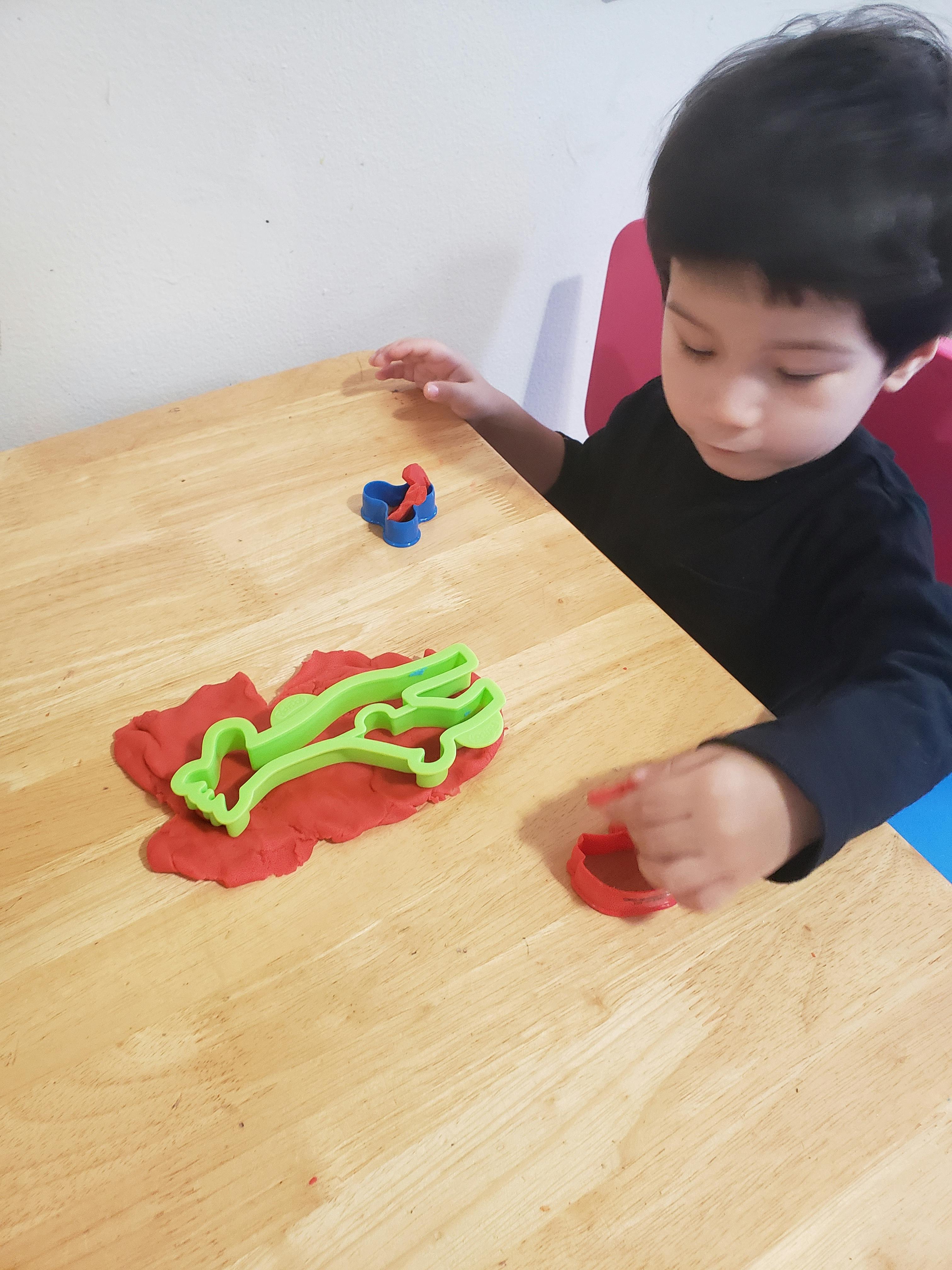 Child playing with red playdough and cookie cutters on a wooden table