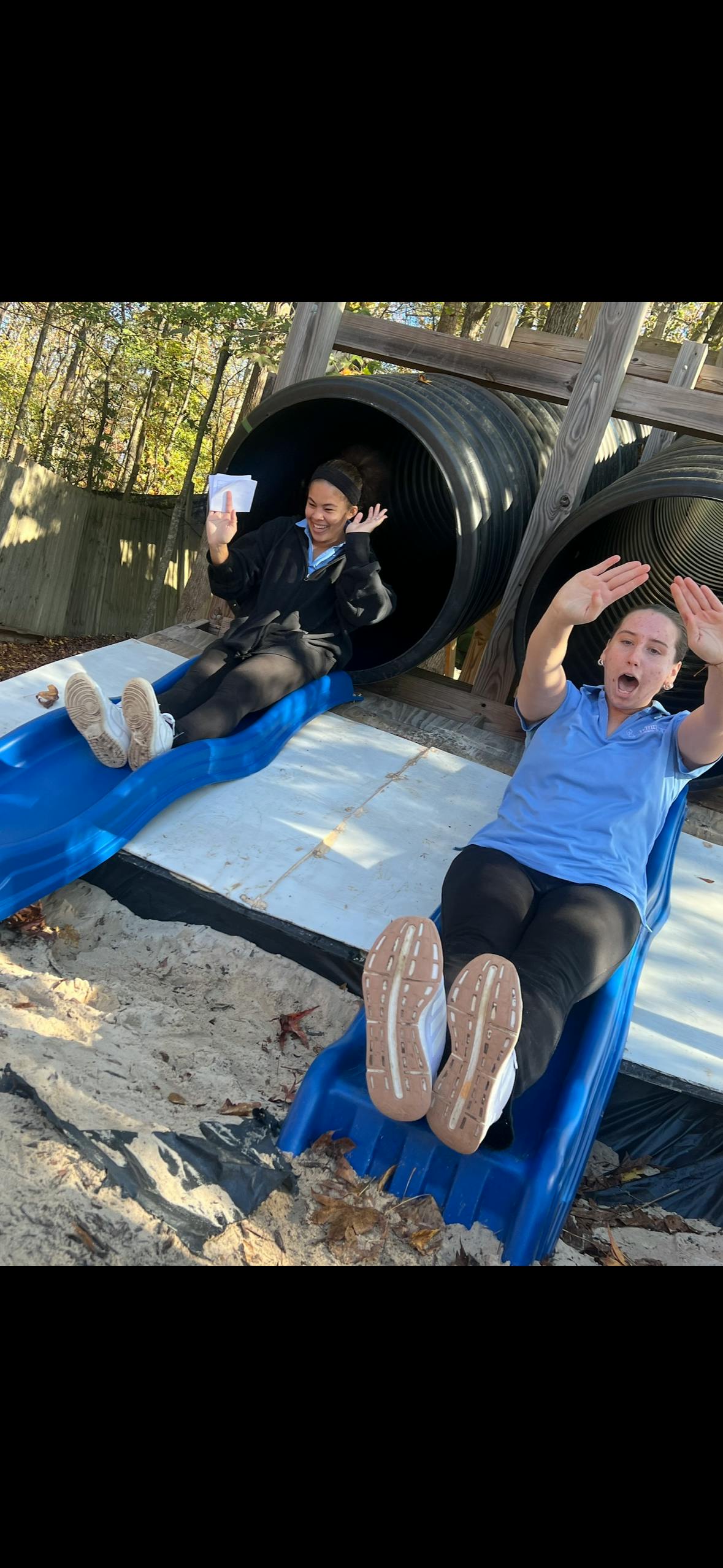 Two people on blue slides coming out of large black tubes